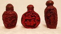Front view of three intricately carved red Chinese snuff bottles showing detailed relief scenes and textured stoppers.