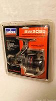 Front angled photo of the Daiwa BW2055 AutoCast graphite fishing reel in unopened original blister package with dust on packaging surface.