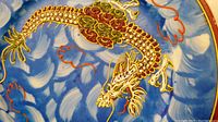 Close-up of hand-painted gold and red dragon on blue and white cloudy background on porcelain plate.