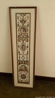 Full view of the tall, narrow framed artwork against a wall, showing the entire piece with classical and mythological decorative elements.