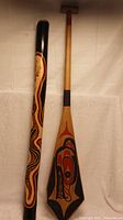 Full view of didgeridoo and paddle standing against a neutral backdrop showing design details and overall condition.