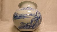 Front view of large antique Korean vase showing cobalt blue painted mountain landscape on white porcelain with bulbous shape and flared lip.