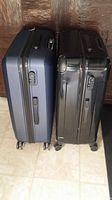 Side-by-side view of blue and black hard shell suitcases showing side handles, wheels and locks.