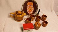 Photo showing brown retro set of 4 mugs, matching teapot, sugar bowl, creamer, red and white metal recipe box, brass hand bell, and Newcastle Brown Ale bar tray in background
