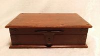 Front view of vintage solid wood box showing rectangular shape, dark reddish-brown finish and central metal lock mechanism.