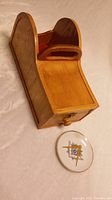 Side angle view of curved wooden box with handle and drawer, and round ceramic dish with Masonic emblem