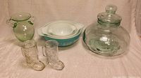 Front view of lot showing three Pyrex nesting bowls, large glass jar with lid, green vase, and two boot-shaped glasses