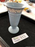 Front view of light blue Wedgwood vase with white classical embossed decoration and fluted body.