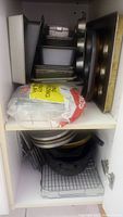 Multiple baking pans including rectangular loaf pans, cake pans, and baking trays stacked inside a cabinet shelf with a large bag of baking mix.