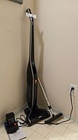 Full view of Hoover LiNX cordless vacuum cleaner standing upright with charger and manual on the floor.