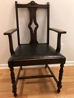Front view of captain's chair showing carved floral rosette on high back, armrests, and black upholstered seat.