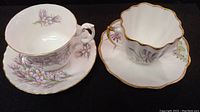 Two vintage bone china tea cups with matching saucers; one Royal Albert Praite Crocus and one Melba Bone China Iris, both with floral decoration and gold trim.