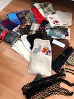 Wide view of assorted scarfs spread out on floor, showcasing a variety of colors and patterns including floral prints.