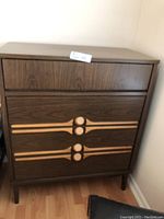 Front view of the mid century modern 4-drawer chest of drawers, showing all drawer fronts and the decorative detail on the handles.