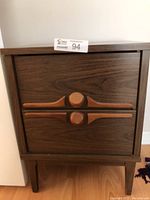 Front view of the mid century modern nightstand showing two drawers with distinctive round and horizontal wood handles.