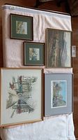 Overview of five framed art pieces laid on white fabric, showing variety of sizes and styles, including prints and sketches.