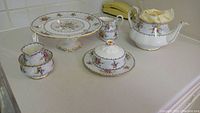 Full set of Royal Albert Petit Point bone china on countertop showing teapot, cake stand, creamer, sugar bowl and covered butter dish