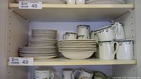 Shelves holding stacks of plates, bowls, and mugs with floral pattern and navy trim.