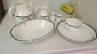 Teapot, creamer, salt and pepper shakers, oval platter, round bowl and one dinner plate arranged on countertop