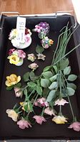 Top view of a collection of porcelain flowers, some on stems, some arranged in small vases, including flower pins.