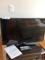 Samsung 30-inch TV placed on a wooden table with remote and user manual.
