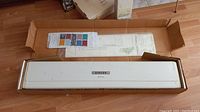 Opened original box showing white metal machine bed and carriage alongside pattern chart and instruction sheet.