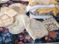 Overview of assorted lace doilies and tablecloths piled together on a floral fabric background in cream, white, and beige colors.