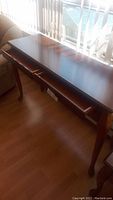 Front angle view of wooden sofa table against window, showing polished top and curved legs.