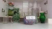 Shelf with multiple glass vases of different shapes and colors including clear, green, and purple vases