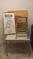 Vintage folding card table with thin metallic legs and black protective covers on feet, placed on tiled floor.