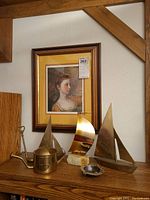 Full scene showing framed portrait above shelf with brass sailboats, watering can, golf club bottle opener, and ashtray arranged on wood shelf.