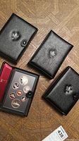 Four black leather-like cases with silver maple leaf emblem containing Canadian Mint uncirculated coin sets.