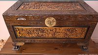 Front view of dark stained carved chest showing floral and bird relief panels and brass lock plate