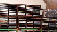 Photo showing multiple CD cases filled with CDs on shelves, five cases total.