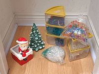 Photo of entire lot showing ceramic Santa planter on chimney, green ceramic Christmas tree, and several containers and bags of plastic lights.