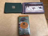 Two Canadian coin sets in their respective cases: a green leather 2004 Specimen set with its box and The Elusive Loon stamp and coin set in a wooden box with a loon image.