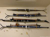 Overview of four ski pairs mounted on wall with bindings and three pairs of poles and wax kit
