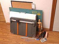 Overview of the drafting set including drafting board, corkboard, cutting mat, artist's mannequin, and office accessories arranged on floor