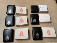 Six black leatherette coin cases with silver Canadian Coat of Arms and matching white presentation boxes with Canadian red crests and note envelopes.