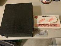 Closed wooden case of Tasco microscope kit beside a box of latex examination gloves and an instruction sheet.