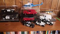 Full lot showing five model cars in plastic cases and three police helicopters, plus three loose cars on the shelf.