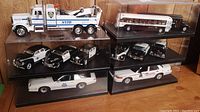 Five clear display cases containing 10 law enforcement and emergency model vehicles, plus one NYPD tow truck.