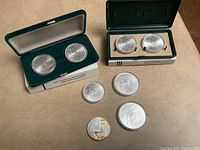 Eight Montreal 1976 Olympic coins arranged with two larger 10 dollar coins in cases and six smaller 5 dollar coins, one loose.