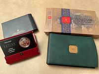 Top-down view showing 2005 Proof Silver Dollar coin in black and red Royal Canadian Mint case and 2002 Golden Jubilee proof set in green folio with outer decorative box.
