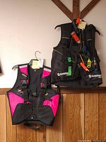 Men's Sherwood Silhouette black inflatable diver's vest hanging next to women's Mares Vector pink and black inflatable diver's vest, both medium size.
