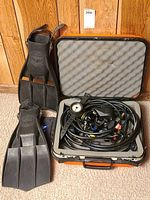 Overall lot showing black Aqua-lung fins with adjustable heel straps alongside regulator set housed in a hard case with foam lining.