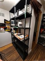 Two black plastic shelving units with items on some shelves, positioned side by side against a wall in a room with wood flooring.