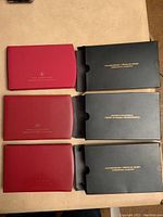 Three closed red Royal Canadian Mint presentation coin cases with black outer sleeves shown on a table.
