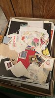 Loose circulated postage stamps mixed with torn paper in a box.