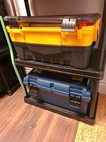 Two stacked plastic tool cases, one yellow/black and one blue/black, on a shelf.